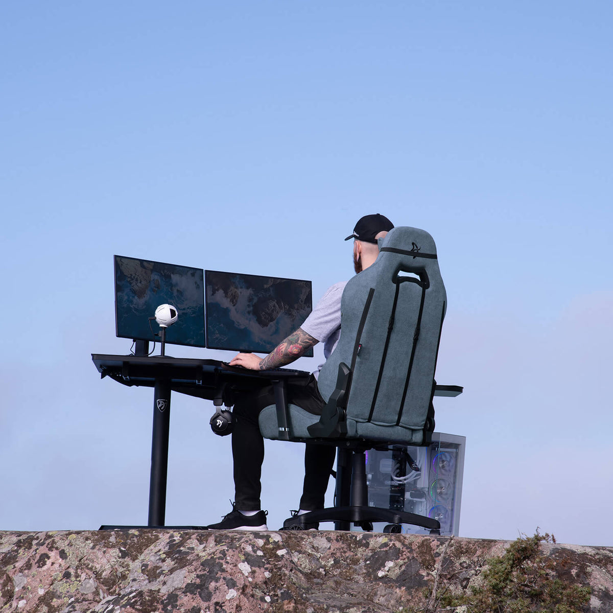 Person in Arozzi Europe Torretta Soft Fabric chair at a desk with dual monitors on a rocky hill.