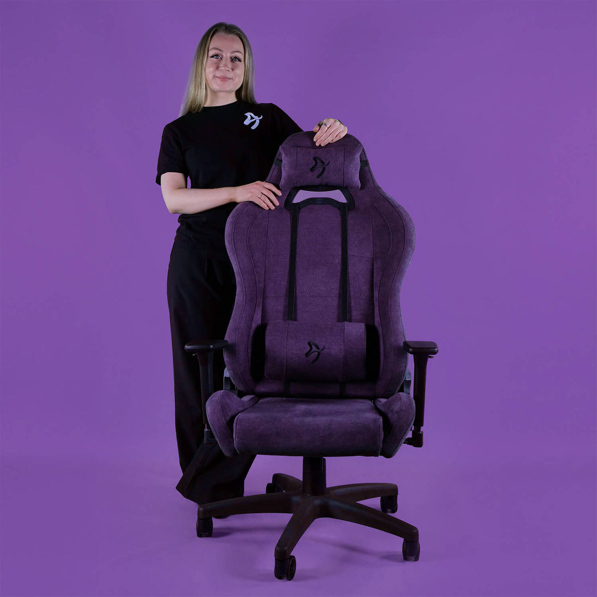 Woman in black stands by a large purple Arozzi Europe Torretta Soft Fabric chair, purple background.