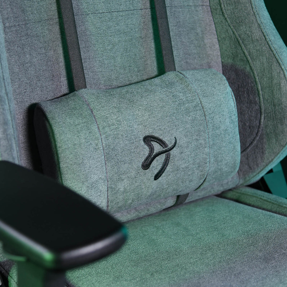 Gray gaming chair with armrest and embroidered pillow featuring a stylized logo.