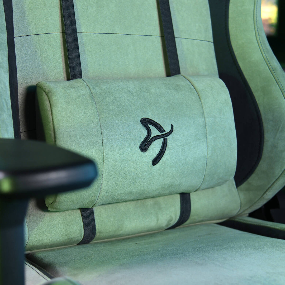 Green gaming chair with black logo and lumbar support pillow, close-up view.