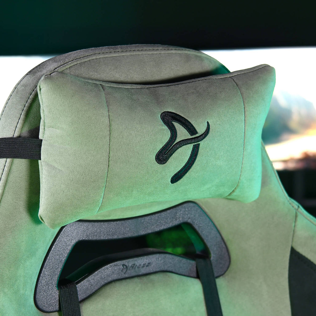 Close-up of a gaming chairs headrest with a black embroidered logo on a green cushion.