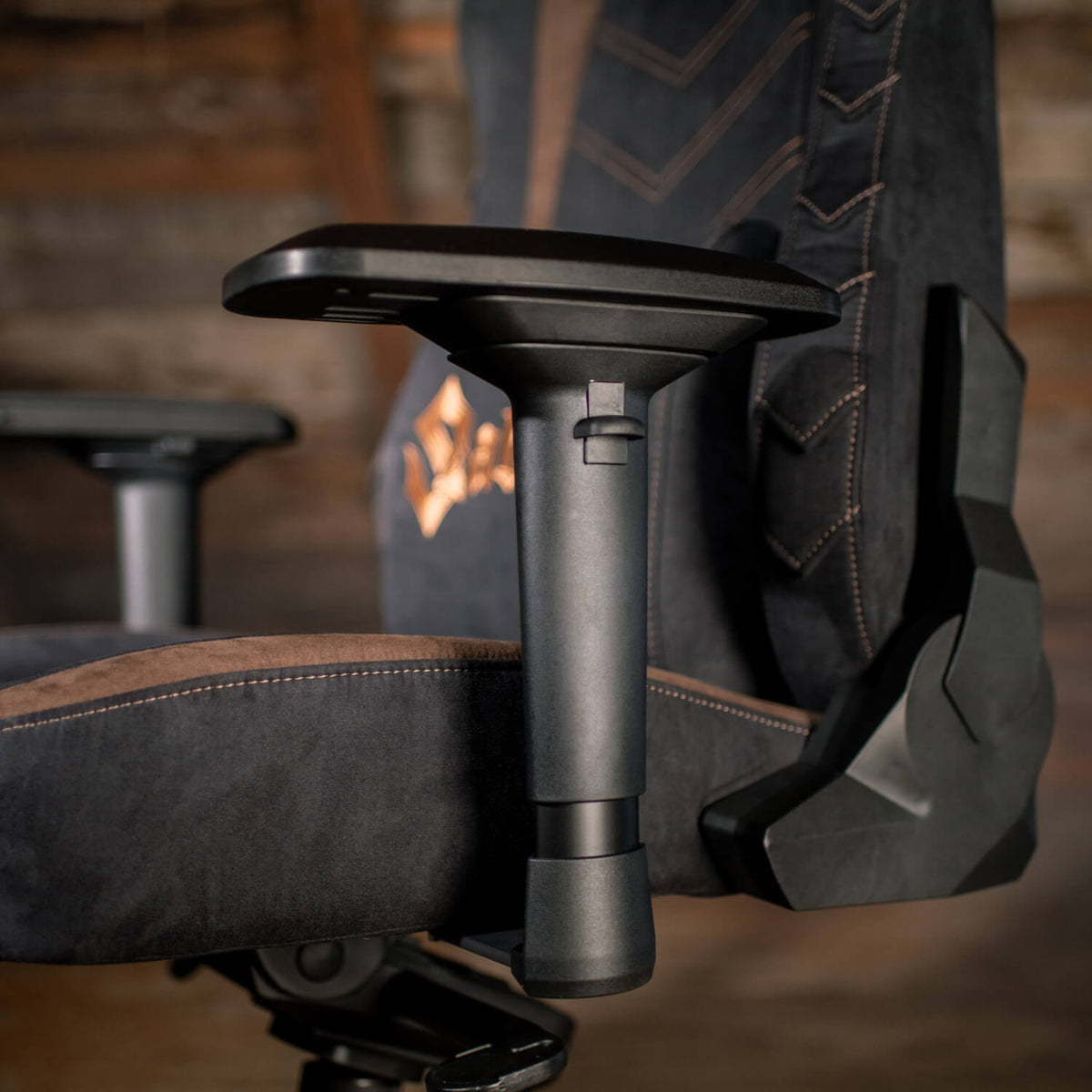 Close-up of a black gaming chair armrest with brown and orange stitching details.