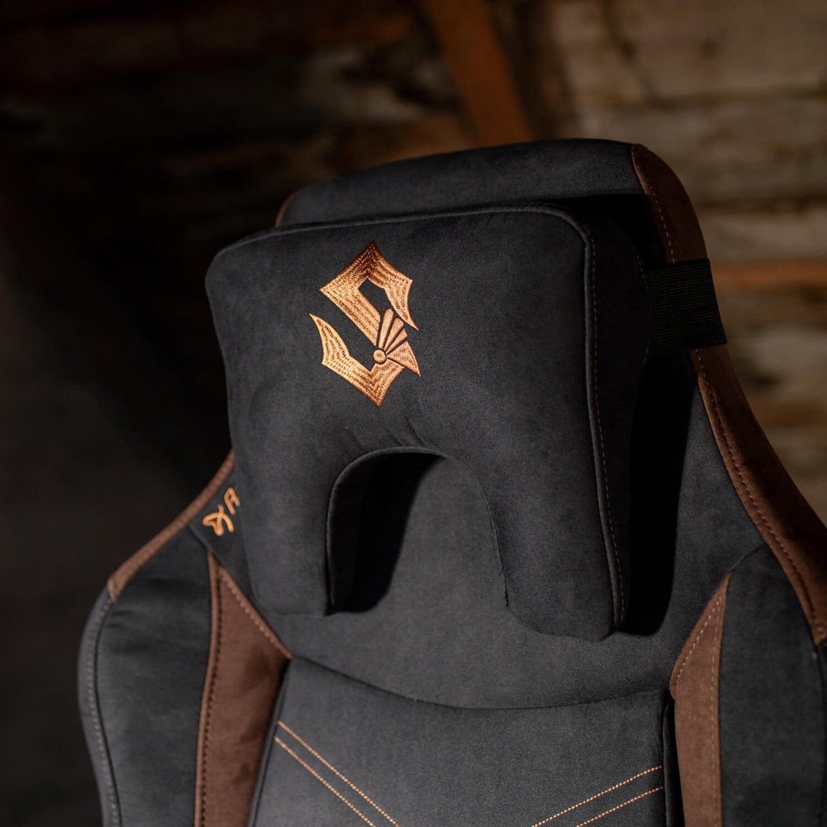 Black and brown gaming chair with a gold emblem on a headrest cushion.