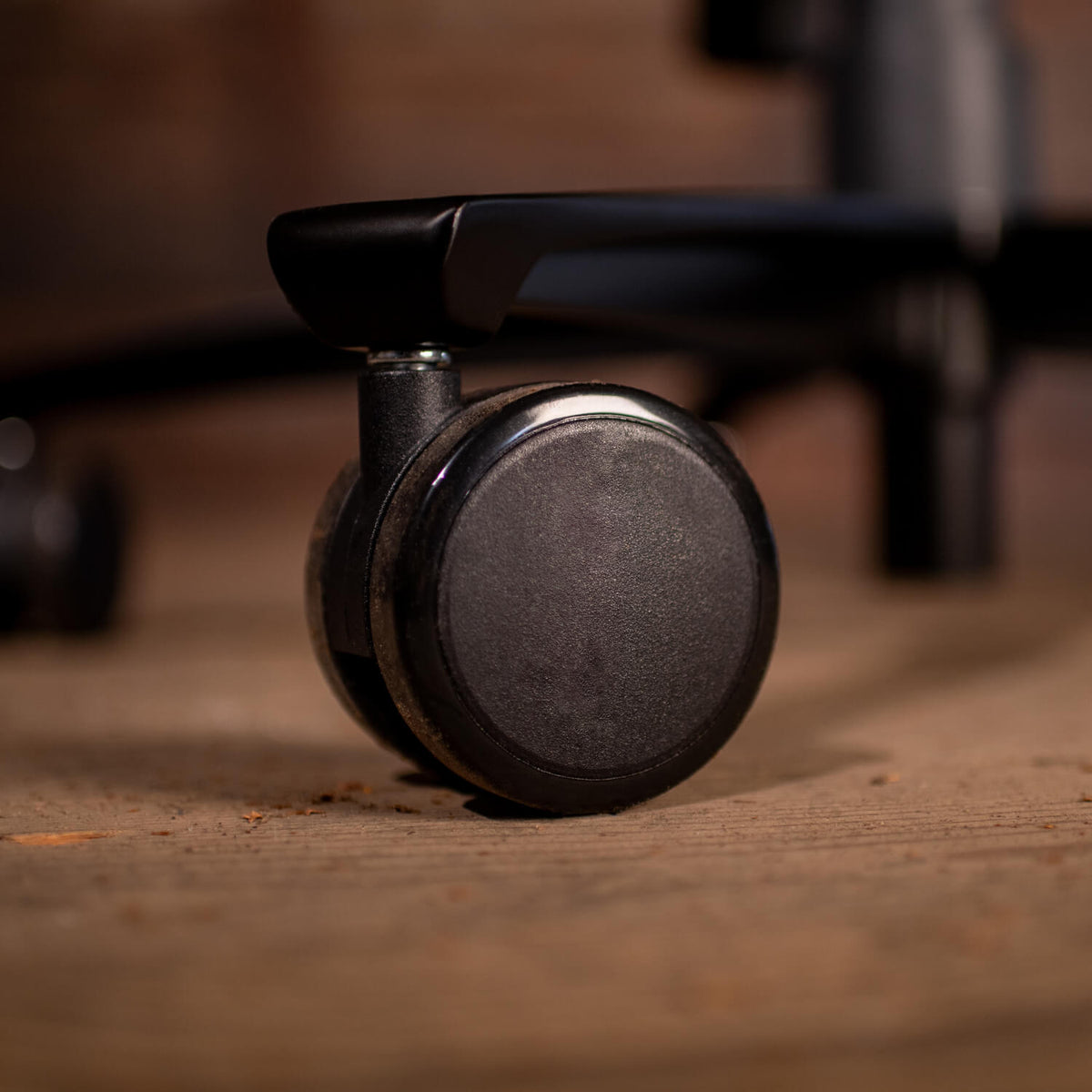 Close-up of a black office chair wheel on a wooden floor.