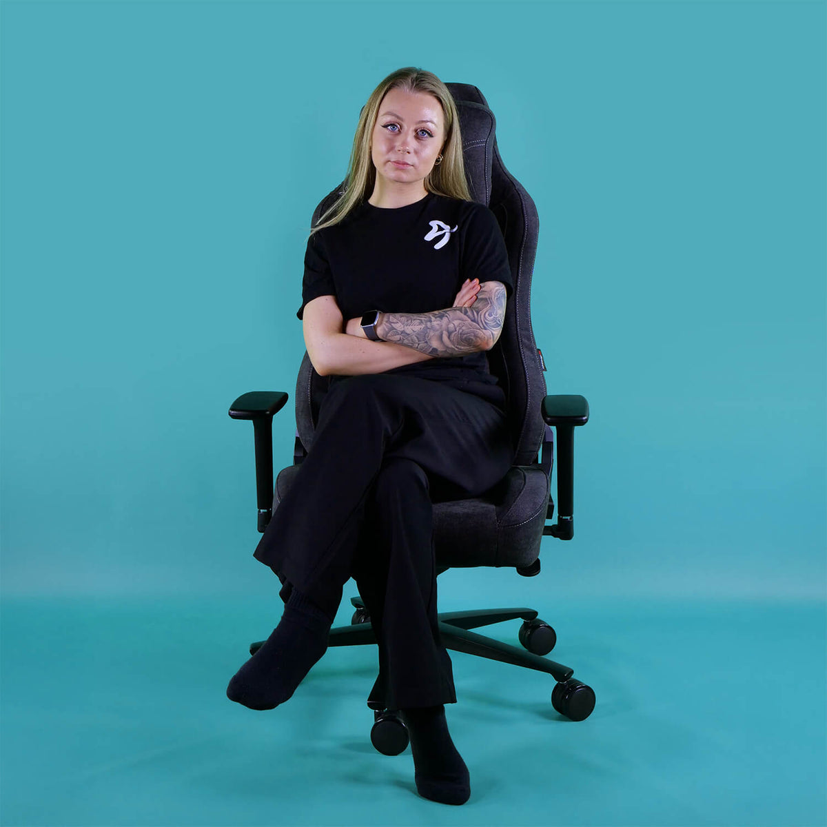 Woman with crossed arms sits on Arozzi Europe Vernazza Soft Fabric chair, teal background.