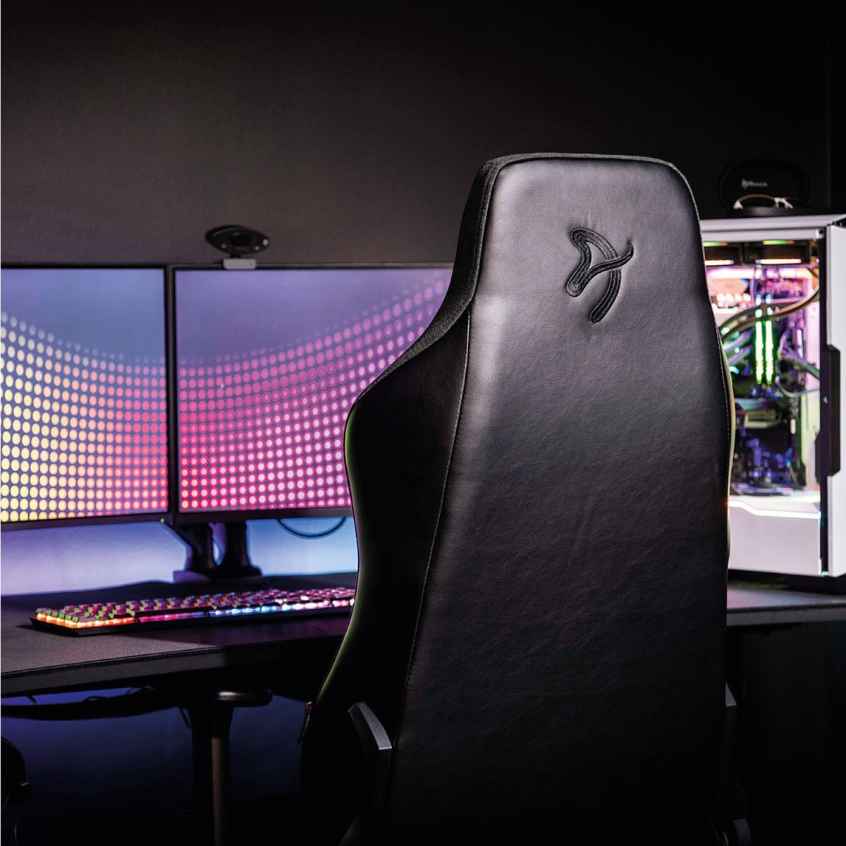 Arozzi Vernazza Vento chair at a dual monitor desk with a lit PC in a dark gaming room.