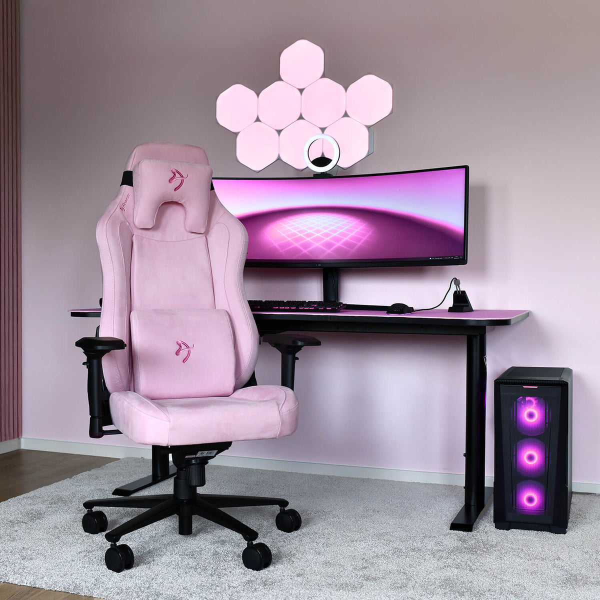 Arozzi Europe Vernazza Supersoft pink chair at a desk with a curved monitor and pink-lit PC.