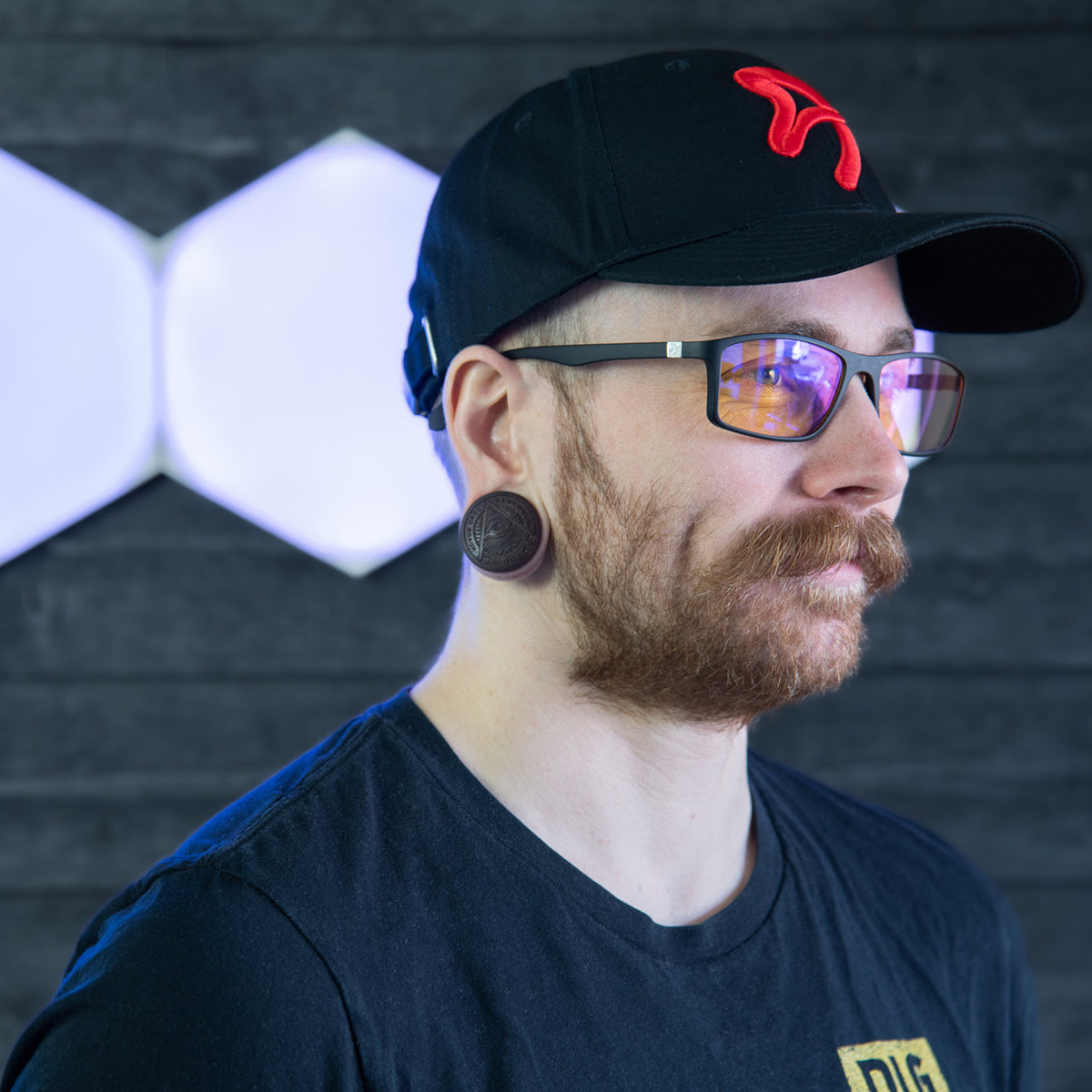 Man wears Arozzi Europe Visione VX-200, cap, and gauges before lit geometric wall pattern.