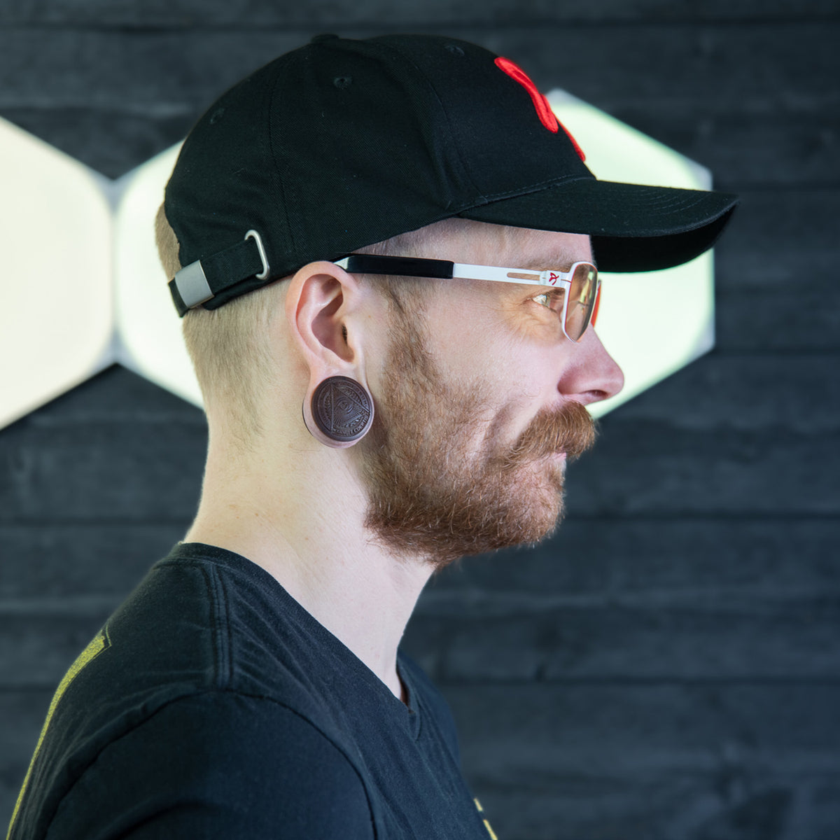 Man in profile wears Arozzi Europe Visione VX-500 blue light glasses, black cap, large ear gauges.