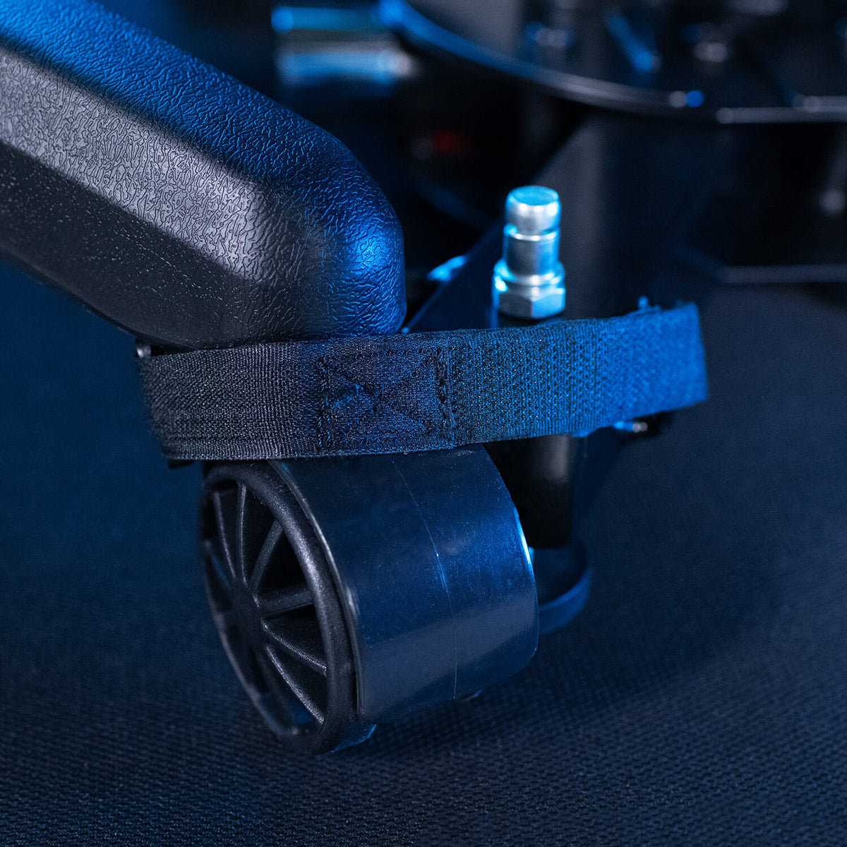 A close-up of a caster wheel secured by a black strap on a dark textured surface.