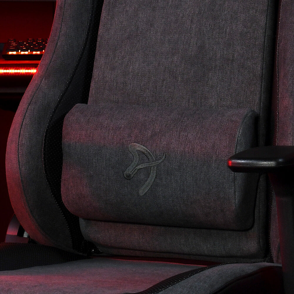 Close-up of a gray gaming chair with a lumbar pillow and red light in the background.