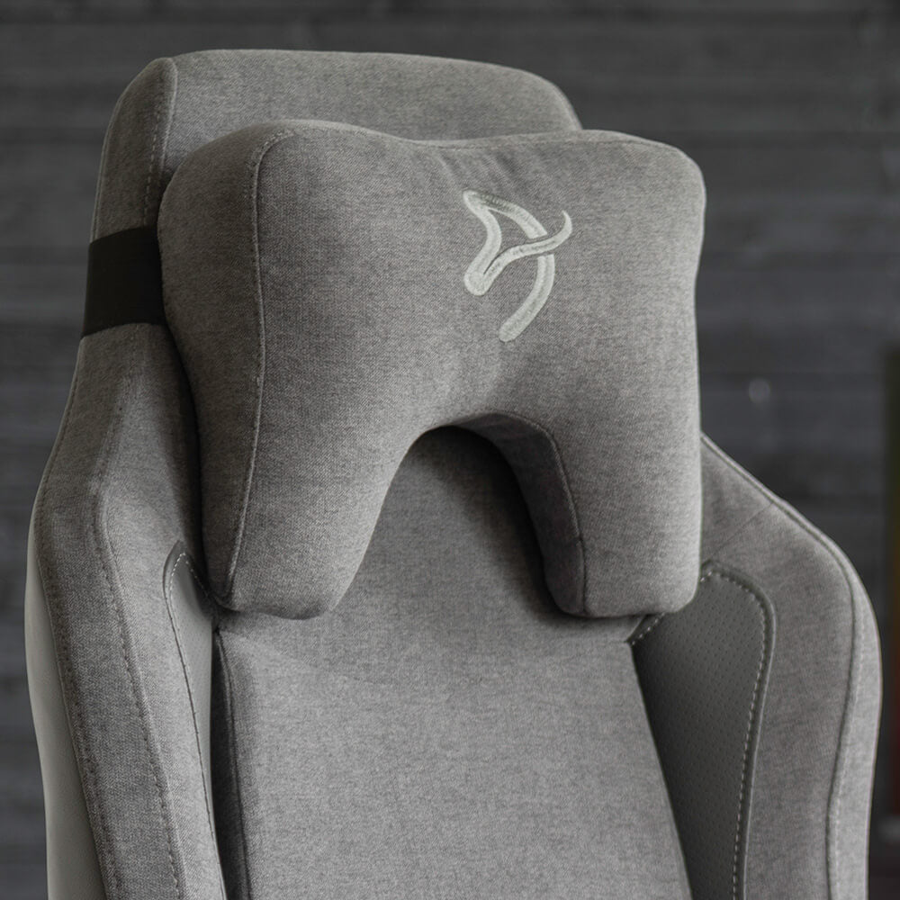 Gray gaming chair with a supportive, cushioned headrest in front of a dark wall.