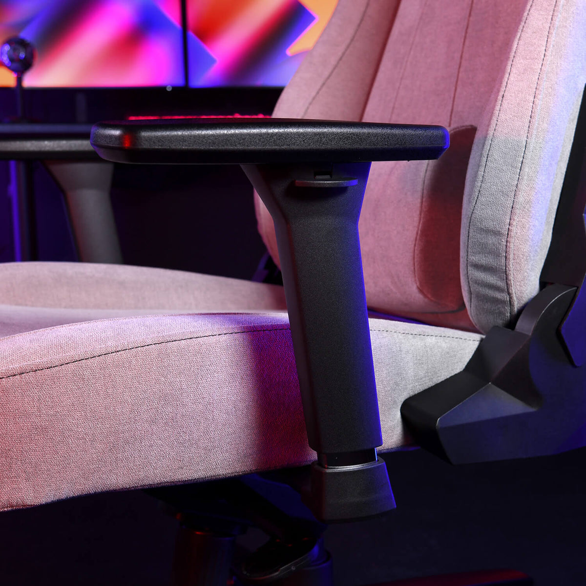 Close-up of Arozzi Europe gaming chair with Armrests - 3D, pink and gray fabric under lights.