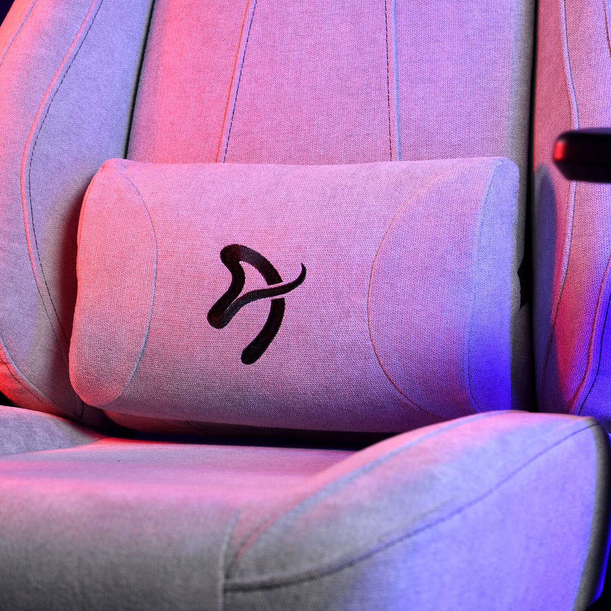 This is a close-up of a light gray chair or seat with a black abstract logo on a lumbar pillow.