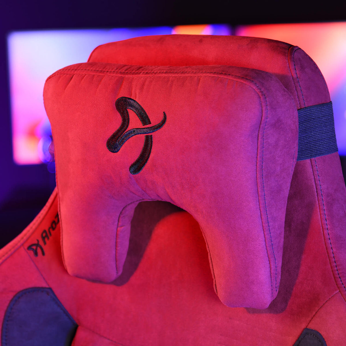Red gaming chair headrest with a black embroidered logo, purple lighting in the background.