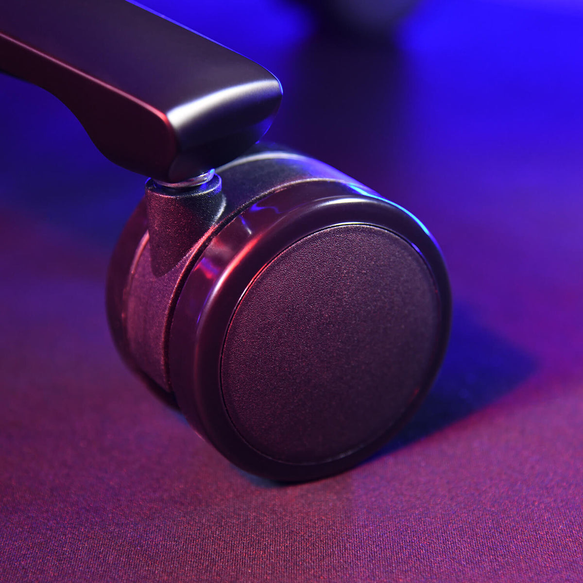Close-up of a black office chair caster wheel on a dark surface with purple lighting.