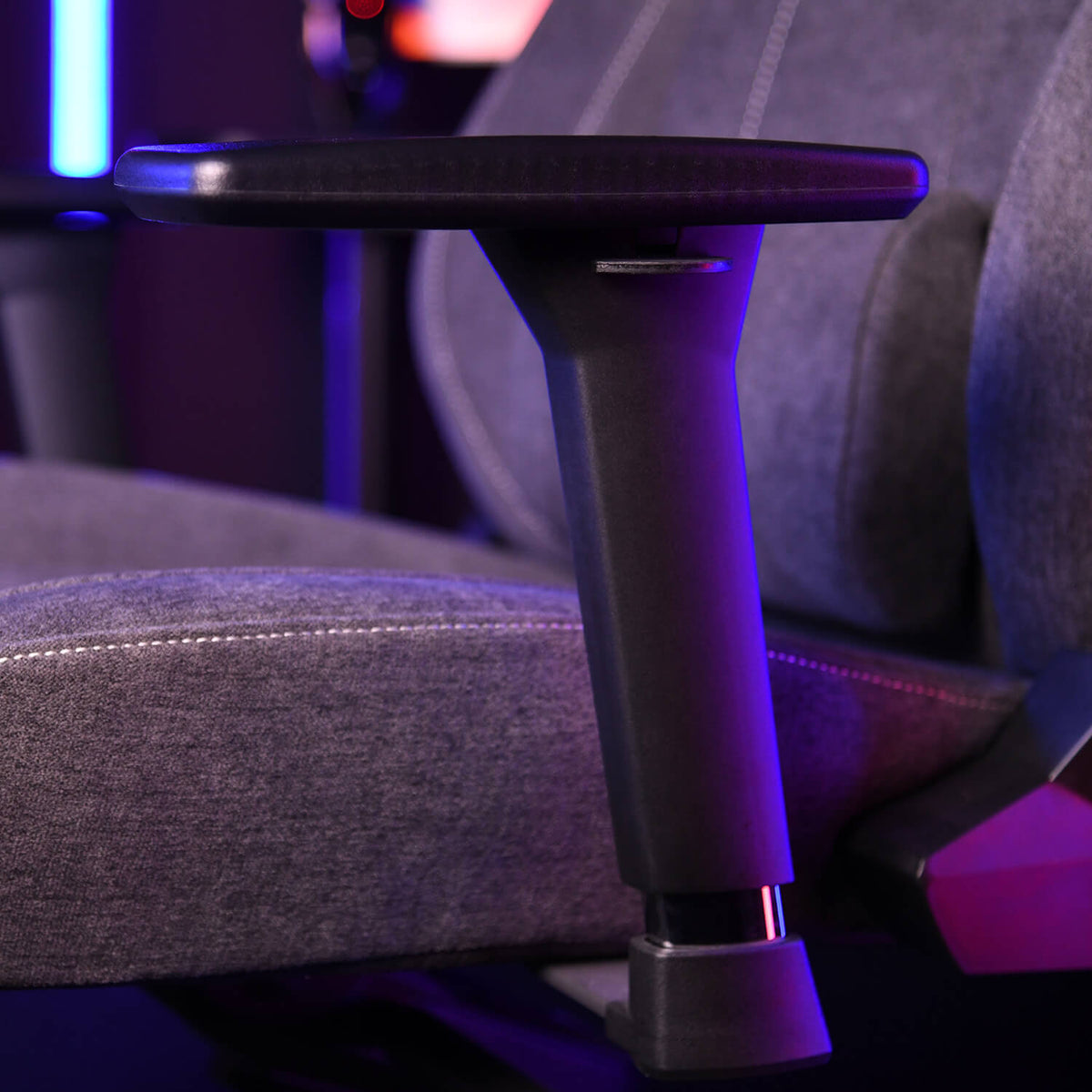 Close-up of a gray gaming chairs adjustable armrest with purple and blue lighting.