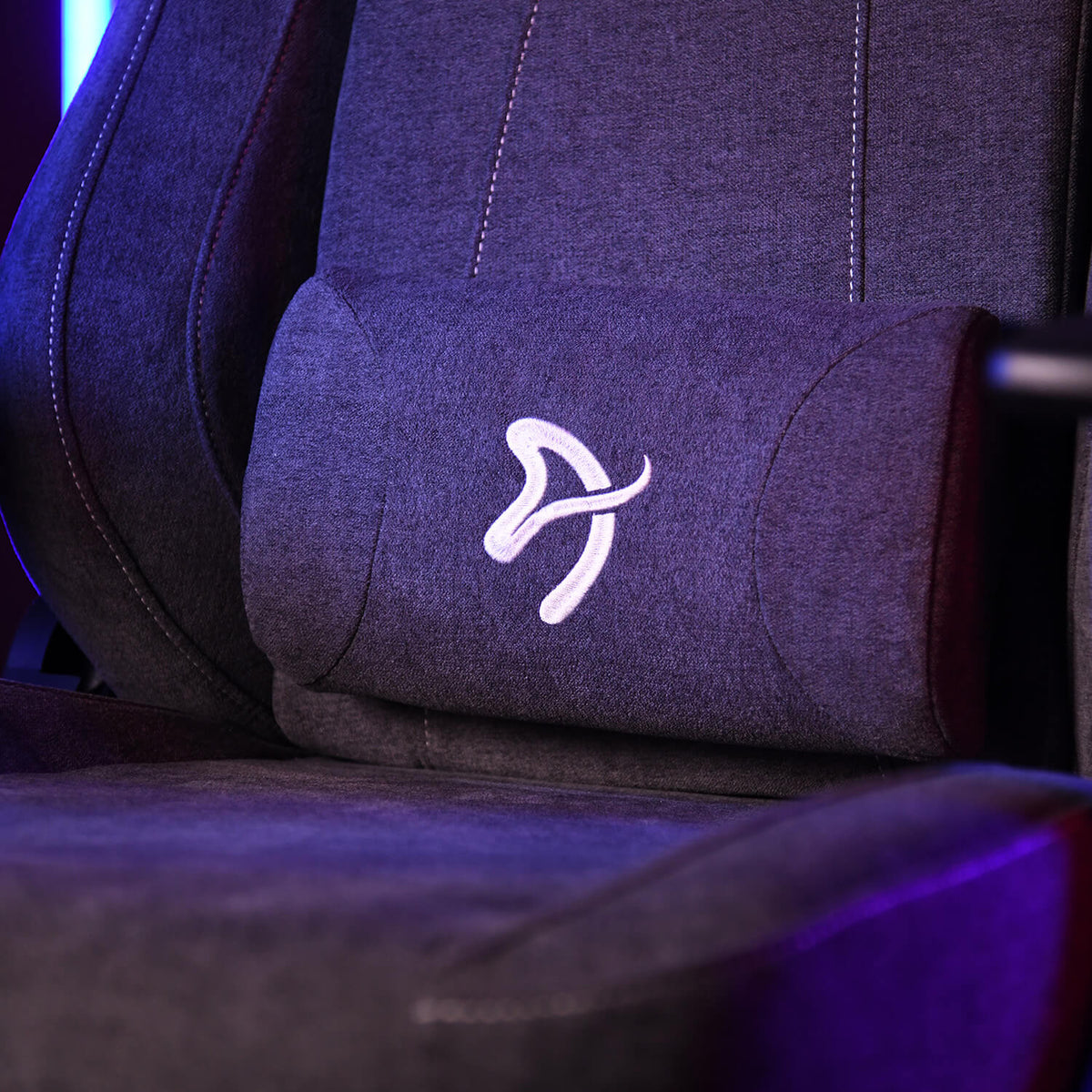 Close-up of a gray gaming chair with a white embroidered logo on the backrest cushion.