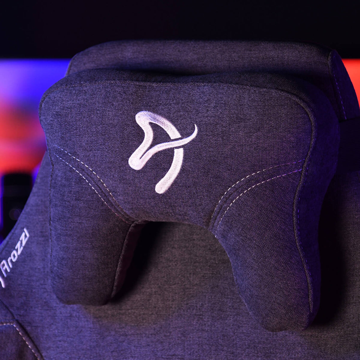 Close-up of a gray gaming chair headrest with white embroidered logo and stitching.