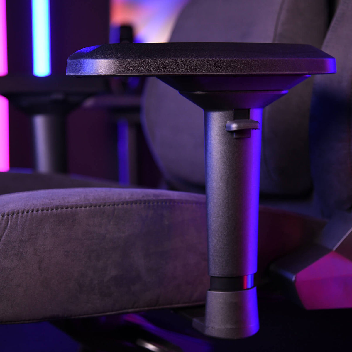 Close-up of a black adjustable armrest on a padded chair with colorful lighting in the background.