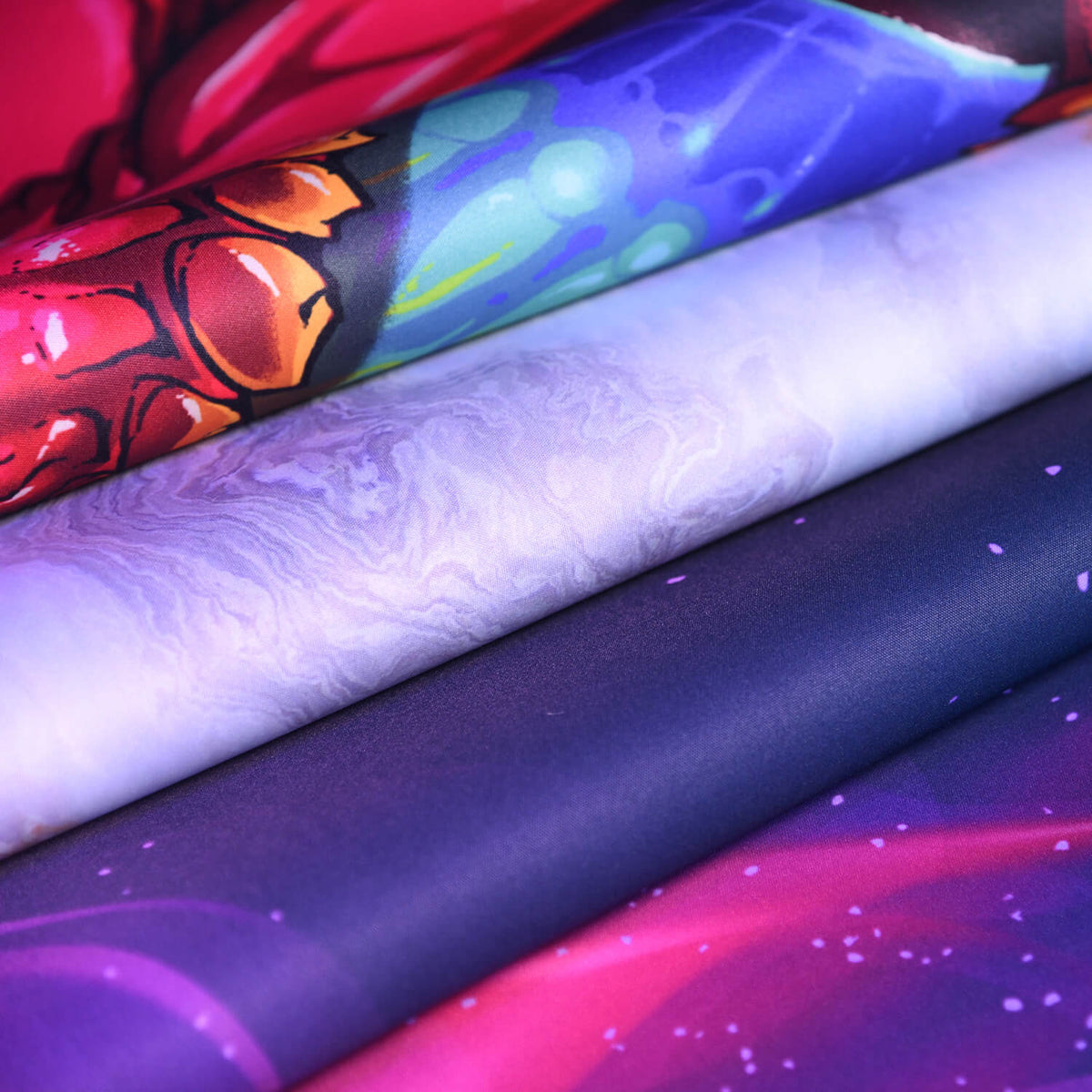 Stacked colorful fabrics with galaxy and abstract patterns, viewed up close.