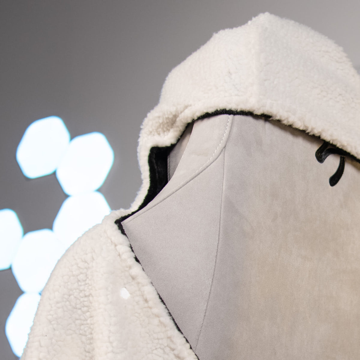 Mannequin wearing a white fleece hooded jacket with blurry lights in the background.