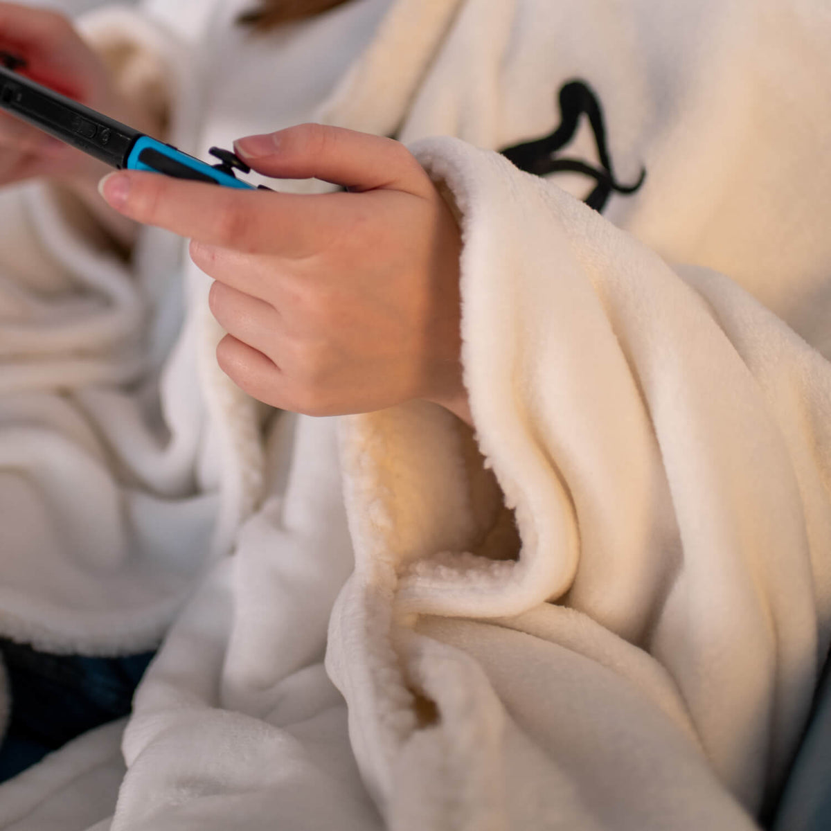 Person in a soft cream blanket holding a gaming console controller with both hands.