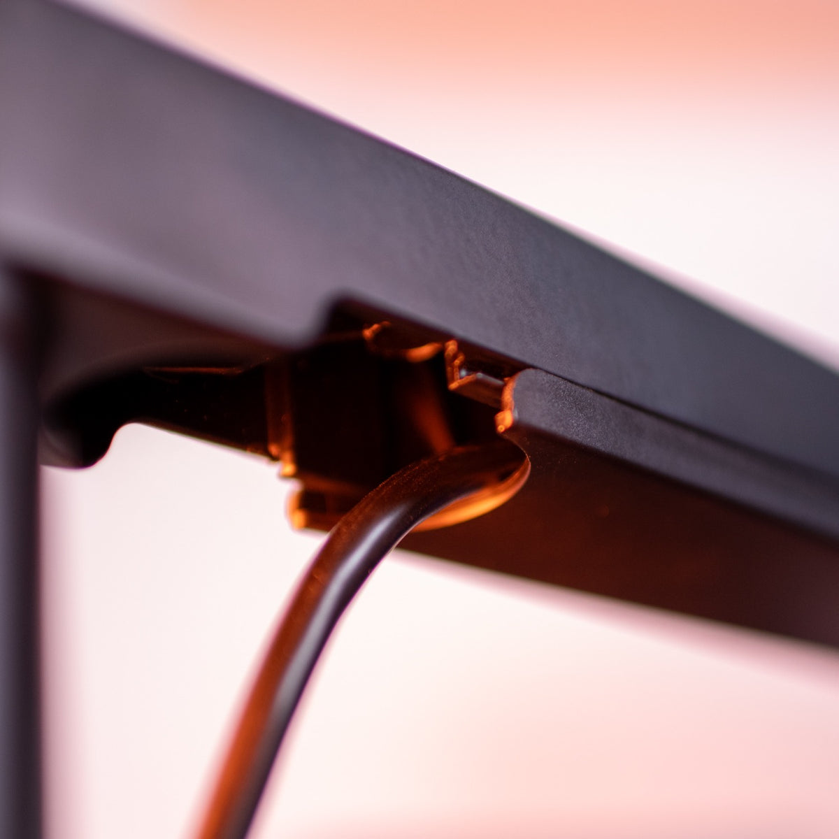 Close-up of a black cable plugged into the underside of a black device, with orange lighting.