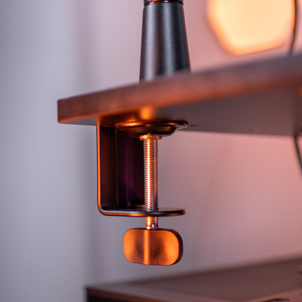 A metal clamp is attached to the edge of a table with warm lighting in the background.