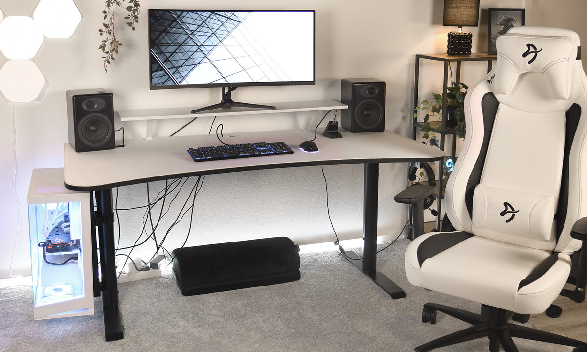 Modern gaming desk setup with monitor, speakers, keyboard, mouse, and white gaming chair.