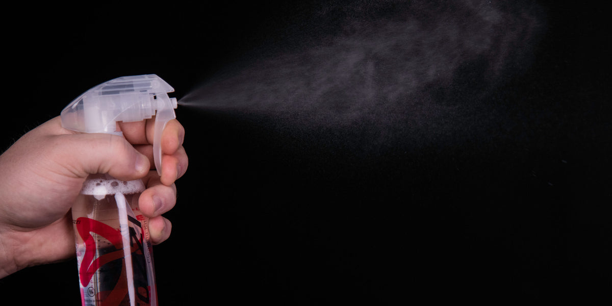 A hand spraying mist from a spray bottle against a black background.