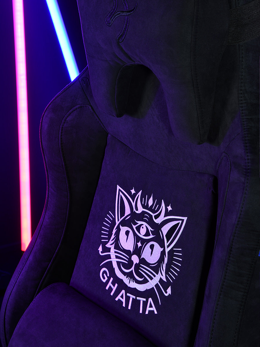 Black gaming chair with neon cat design on cushion, pink and blue light sticks in background.
