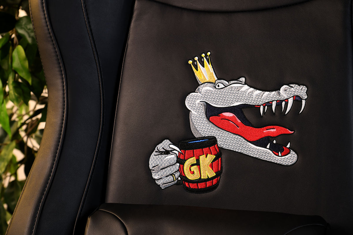 A crowned cartoon alligator embroidered on a chair, holding a red mug labeled GK..
