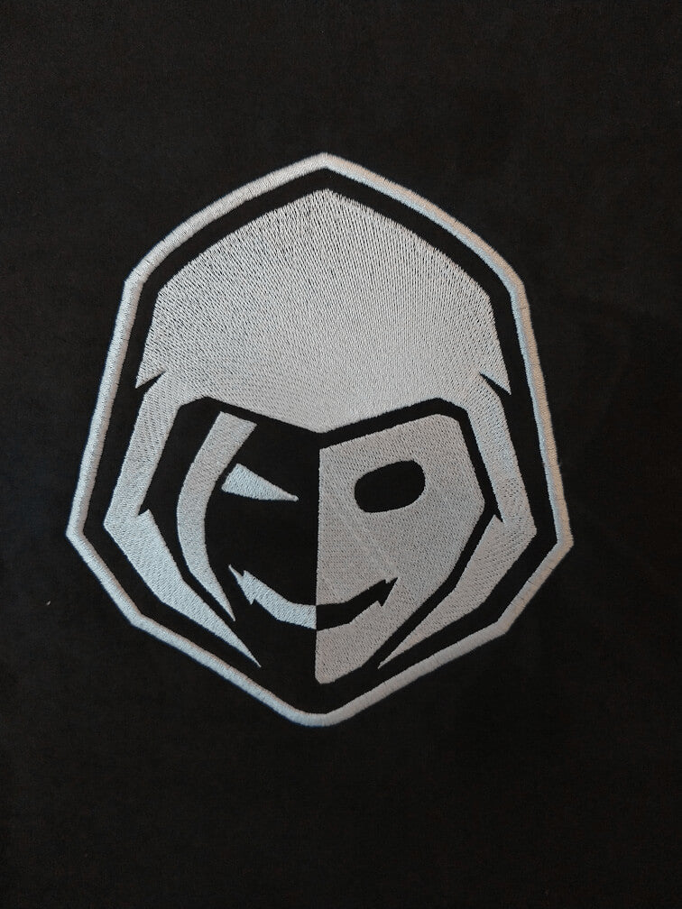 Black and white embroidered patch with a hooded face, half smiling, half shadowed.