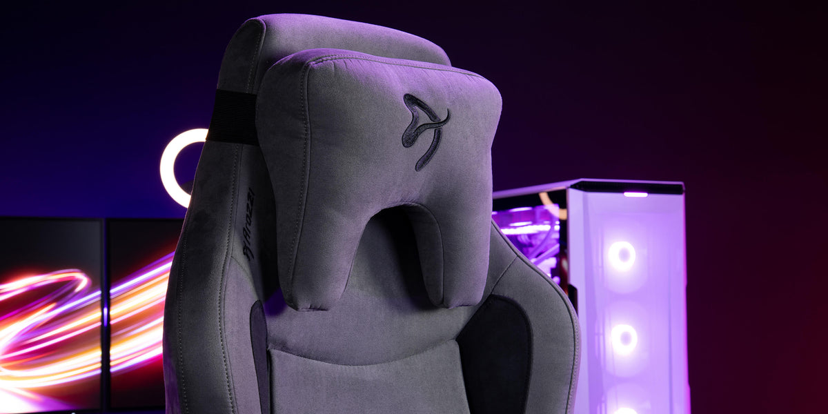 Gray gaming chair with headrest in front of purple-lit PC and monitors.