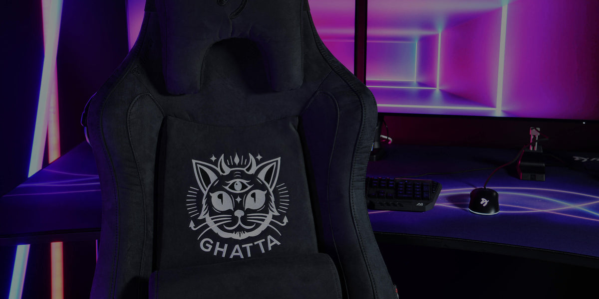 Black gaming chair with a cat logo in front of a desk and pink-purple LED lights.