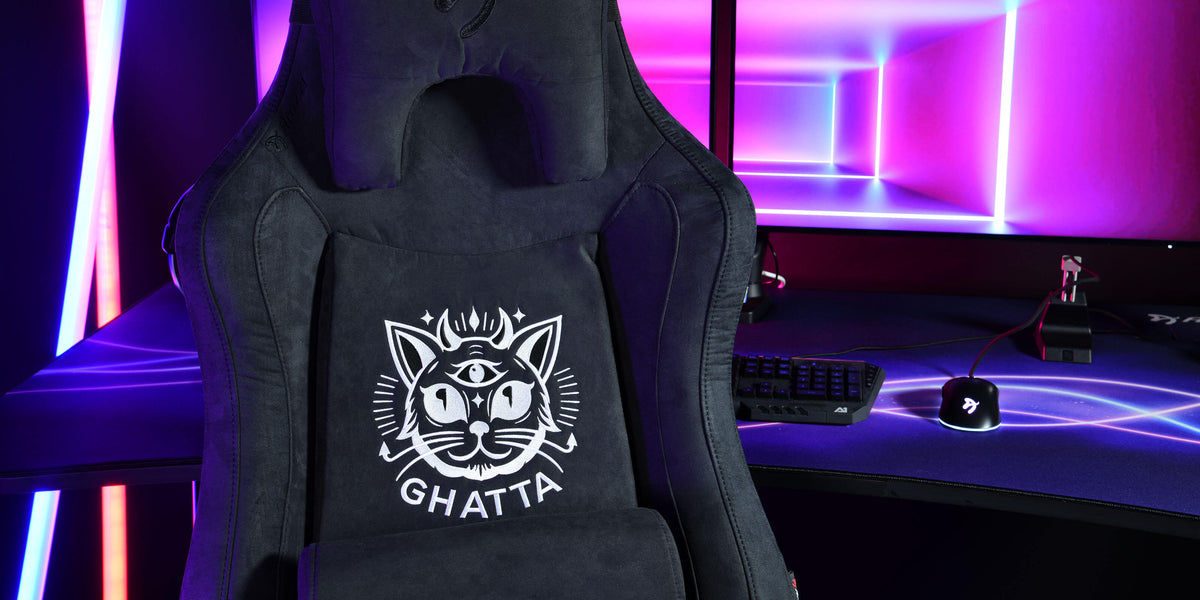 Black gaming chair with a cat logo in front of a computer setup with neon purple lights.