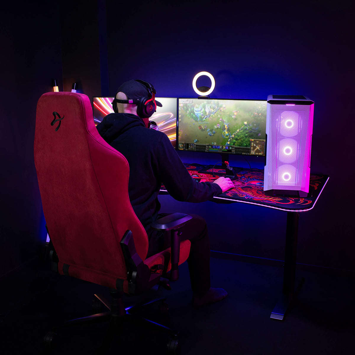 Person gaming at a desktop setup with colorful lights and dual monitors in a dark room.